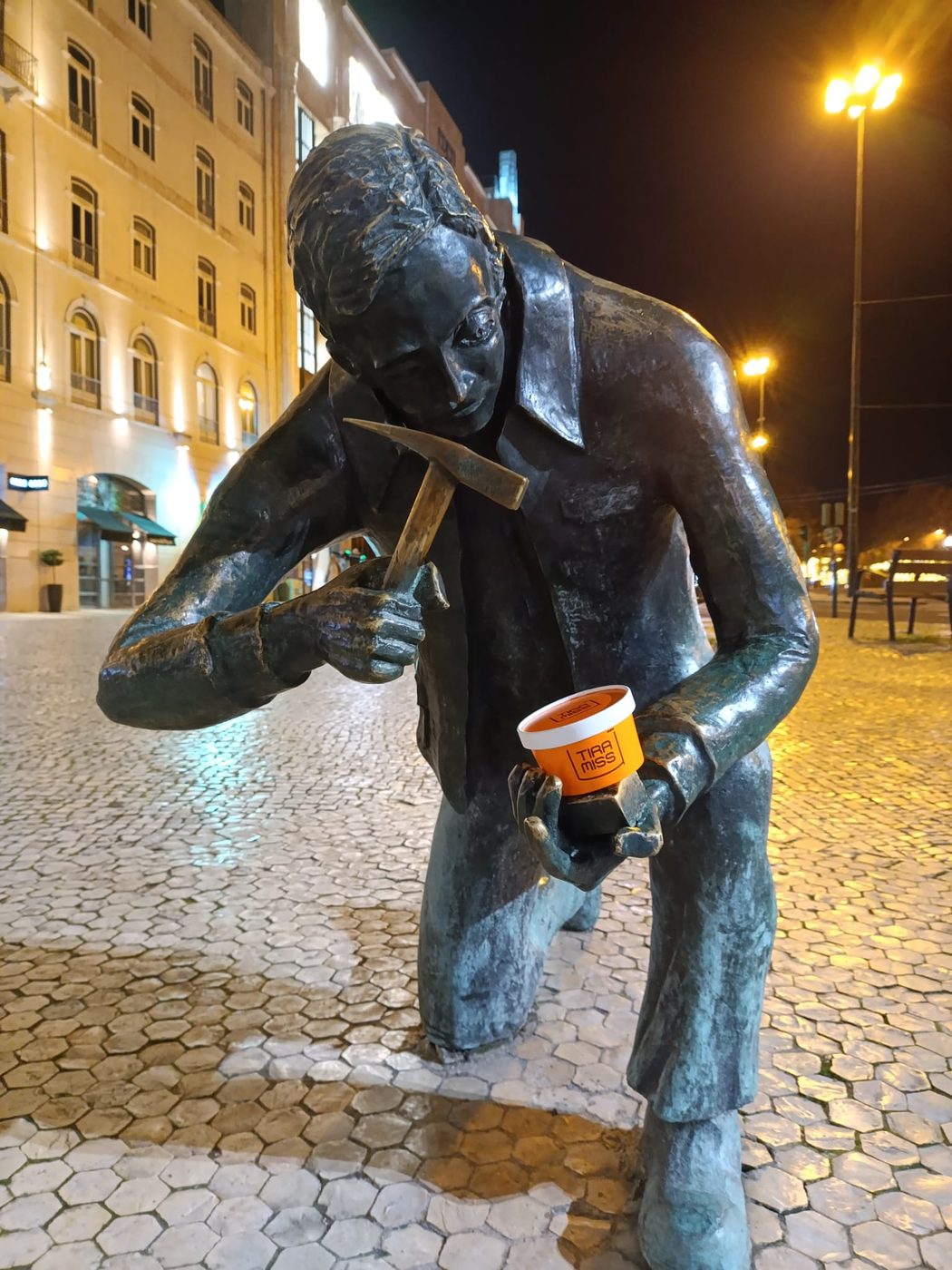 À noite, a estátua do calceteiro segura uma copa TiraMissÙ