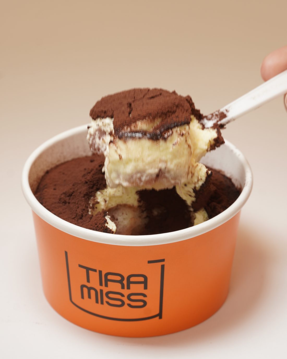 Uma colherada de tiramisù Clássico a sair da copa, com as camadas de creme e cacau à vista