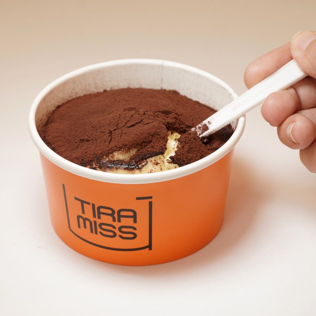Tiramisù gelado na copa laranja, com uma colher a revelar o creme sob o cacau